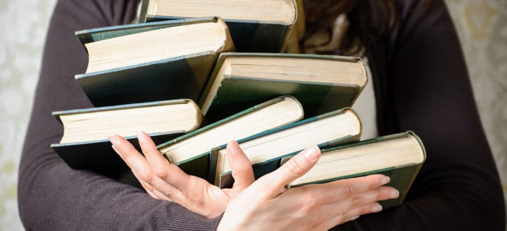 The Stigma of Self-Published Authors blog featured image woman holding onto a stack of books