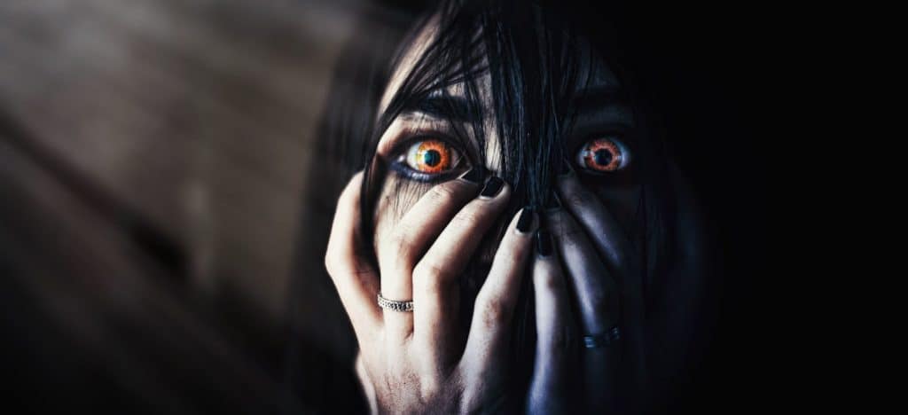 Writing Evil Characters blog post featured image spooky girl with yellow eyes and hands over her mouth