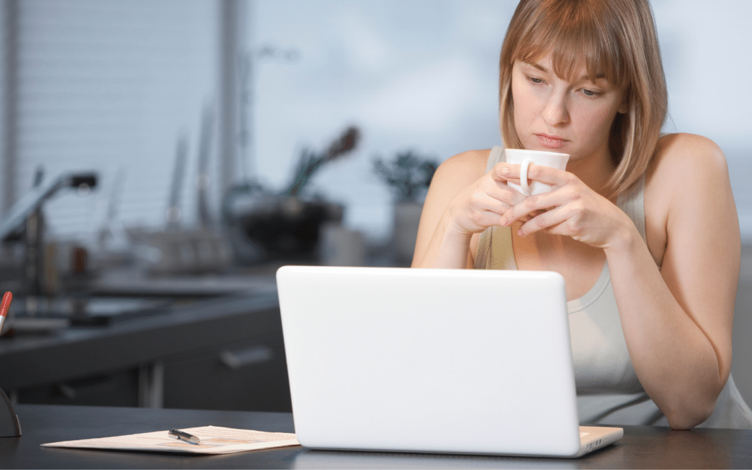 4 Things to Consider when Setting Your Rates as a Freelance Writer image featuring woman sitting in front of her laptop looking pensive while holding a cup of coffee