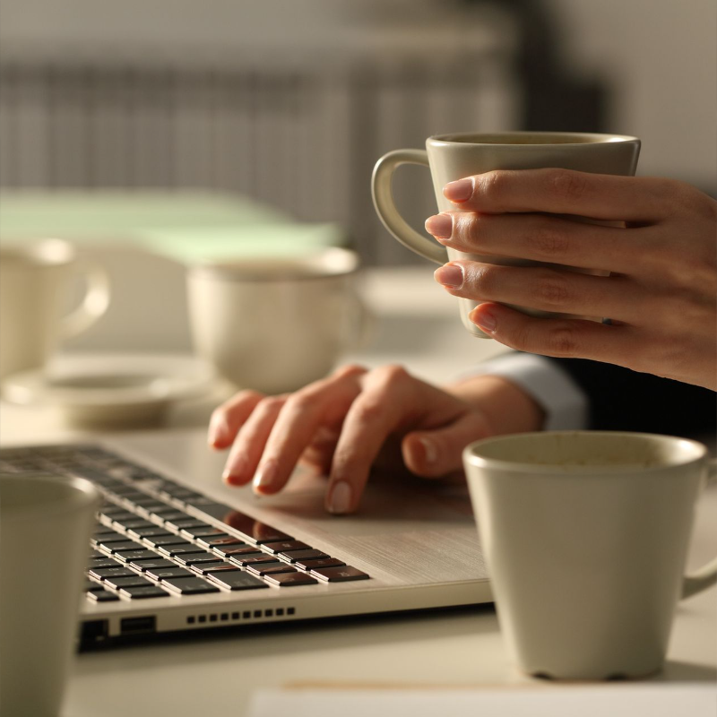 Woman using a laptop while holding a cup of coffee and surrounded by coffee mugs emulating the long and tiresome job of ghostwriting for the blog post "Why a Ghostwriter with more than 15 years of professional experience would take James Patterson's Master Class" 